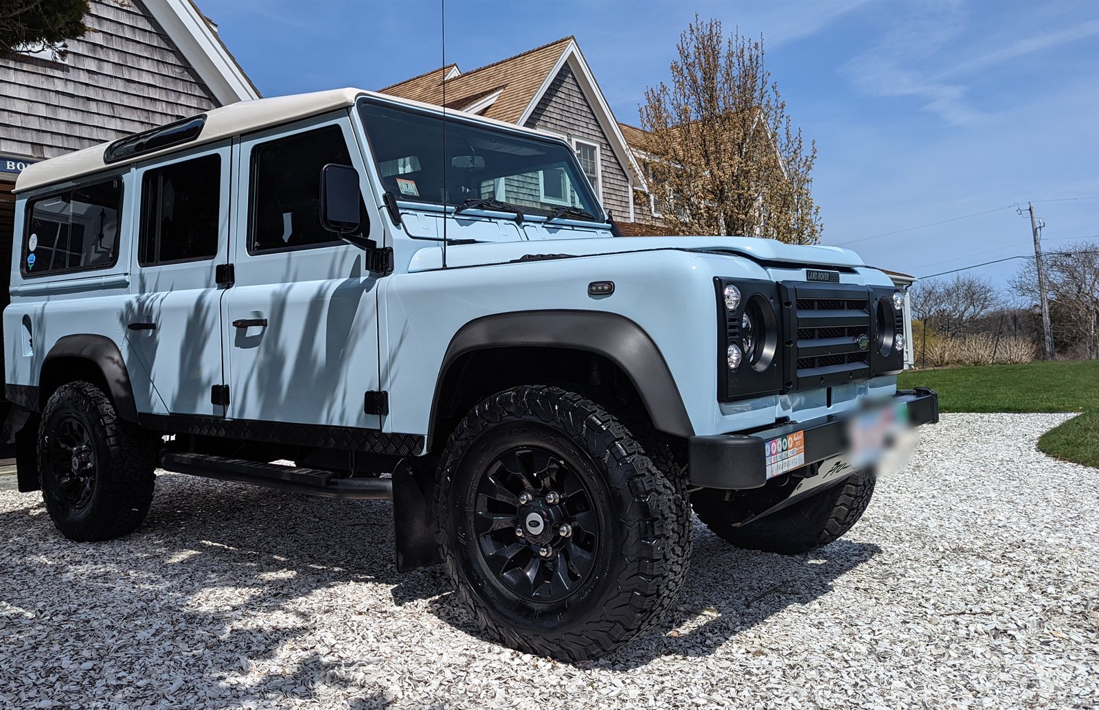 Freshly detailed Land Rover Defender on a crushed-shell driveway beside a cedar-shingled Nantucket home